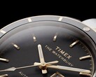Zbliżenie na zegarek Timex Waterbury Heritage Automatic z czarną tarczą, ukazujące jego fasetowane, luminescencyjne wskazówki, znaczniki godzin, wyświetlacz dnia i daty oraz czarną ramkę.