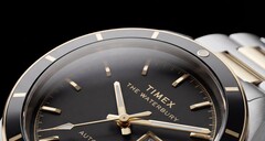 Zbliżenie na zegarek Timex Waterbury Heritage Automatic z czarną tarczą, ukazujące jego fasetowane, luminescencyjne wskazówki, znaczniki godzin, wyświetlacz dnia i daty oraz czarną ramkę.