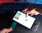 Yu z kanału YouTube Better Gaming trzyma Nintendo Switch 2 w jednej ręce, a w drugiej zielony adapter PCB open-source, próbując włożyć go do gniazda microSD Express urządzenia (źródło obrazu: Better Gaming via YouTube)