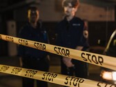 Dwóch policjantów stojących nocą za żółtą taśmą z napisem Stop