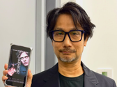 Hideo Kojima pokazujący plakat Physint na swoim telefonie
