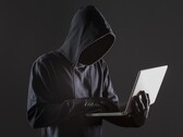Zakapturzony haker obsługujący laptopa na ciemnym tle.