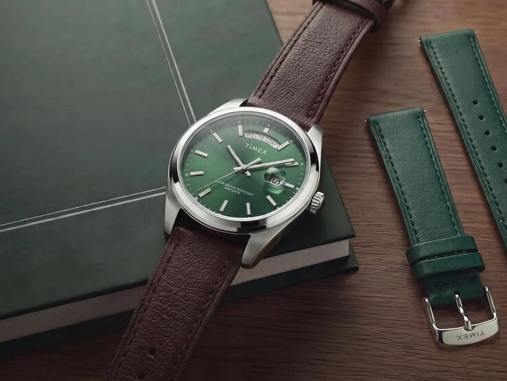 Timex Legacy Day and Date z zieloną tarczą i brązowym skórzanym paskiem zaprezentowany na ciemnozielonej książce obok wymiennego zielonego skórzanego paska.