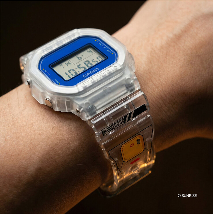 Casio G-Shock x Mobile Suit Gundam DW-5600GM26-7DR noszony na nadgarstku, z kopertą i paskiem z przezroczystej żywicy, niebieskim obramowaniem bezela i grafiką inspirowaną Gundam na pasku.