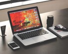 MacBook Pro na ciemnym biurku obok smartfona, okularów i notesu
