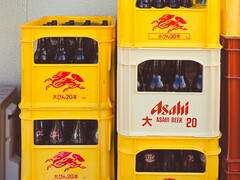 Ułożone w stos żółto-białe plastikowe skrzynki wypełnione butelkami piwa Asahi z japońskim tekstem i czerwonym logo. (Źródło zdjęcia: Alazne Lazcano via Pexels)