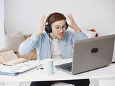 Mężczyzna w słuchawkach unoszący ręce z frustracji przed laptopem