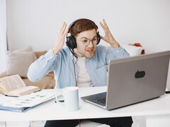 Mężczyzna w słuchawkach unoszący ręce z frustracji przed laptopem