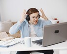 Mężczyzna w słuchawkach unoszący ręce z frustracji przed laptopem