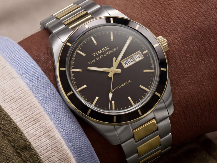 Dwukolorowy zegarek Timex Waterbury Heritage Automatic z czarną tarczą, noszony na nadgarstku, z widocznym wskaźnikiem dnia tygodnia i daty oraz złotymi akcentami.