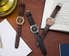 Trzy zegarki marki Citizen Rolan ułożone na drewnianym biurku obok notesu, długopisu, lampy i otwartej książki, w tym model AW2110-14Z z tarczą w kolorze łososiowym.