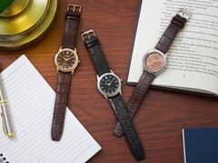 Trzy zegarki marki Citizen Rolan ułożone na drewnianym biurku obok notesu, długopisu, lampy i otwartej książki, w tym model AW2110-14Z z tarczą w kolorze łososiowym.