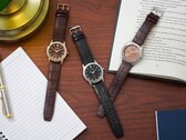 Trzy zegarki marki Citizen Rolan ułożone na drewnianym biurku obok notesu, długopisu, lampy i otwartej książki, w tym model AW2110-14Z z tarczą w kolorze łososiowym.
