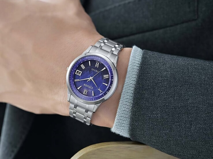 Citizen Exceed CB1140-79L na nadgarstku, prezentujący niebieską tarczę, kopertę w srebrnym kolorze i zintegrowaną tytanową bransoletę na tle ciemnej marynarki.
