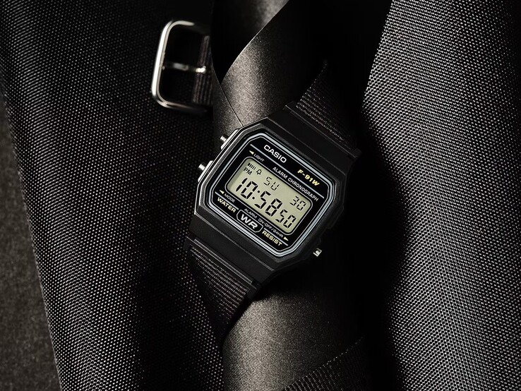 Cyfrowy zegarek Casio F-91WF-1A z czarną kopertą, czarnym paskiem z tkaniny plecionej i srebrnymi akcentami, sfotografowany na ciemnym, teksturowanym tle.