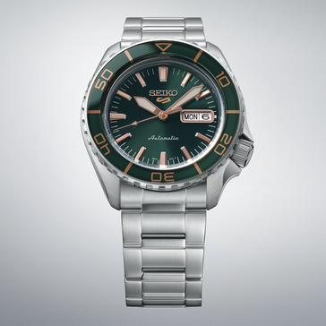 Seiko 5 Sports SKX HDB005 z ciemnozieloną tarczą, dopasowaną zieloną lunetą, wskazówkami i indeksami w kolorze różowego złota oraz bransoletą ze stali nierdzewnej, pokazany na jasnoszarym tle.