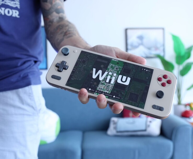 Russ z Retro Game Corps trzymający konsolę przenośną Ayaneo Pocket S2 z emulatorem Wii U, z urządzeniem pokazanym w widocznym miejscu w salonie. (Źródło zdjęcia: Retro Game Corps)