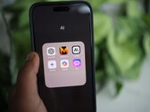Dłoń trzyma smartfon, na którym widoczny jest folder o nazwie „AI” zawierający aplikacje, w tym Gemini, ChatGPT i Claude