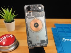 Przezroczysty iPhone Air pokazujący wewnętrzne komponenty i miedzianą cewkę ładującą na drewnianym biurku (źródło obrazu: Phone Repair Guru via YouTube)