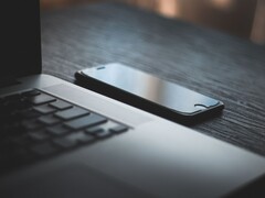 Smartfon leżący obok otwartego laptopa na ciemnym biurku