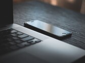 Smartfon leżący obok otwartego laptopa na ciemnym biurku