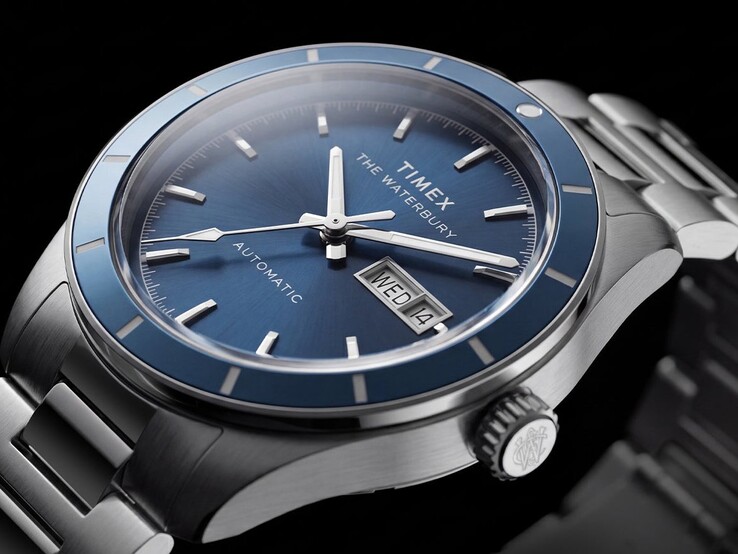 Zbliżenie na zegarek Timex Waterbury Heritage Automatic z niebieską tarczą, ukazujące świecące wskazówki, nakładane znaczniki godzin oraz wyświetlacz dnia tygodnia i daty.