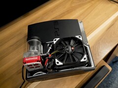 Niestandardowe chłodzenie wodne PlayStation 3 z czerwoną pompą SysCooling i dużym czarnym wentylatorem zamontowanym wewnątrz obudowy, umieszczone na drewnianym biurku. (Źródło zdjęcia: Zac Builds via YouTube)