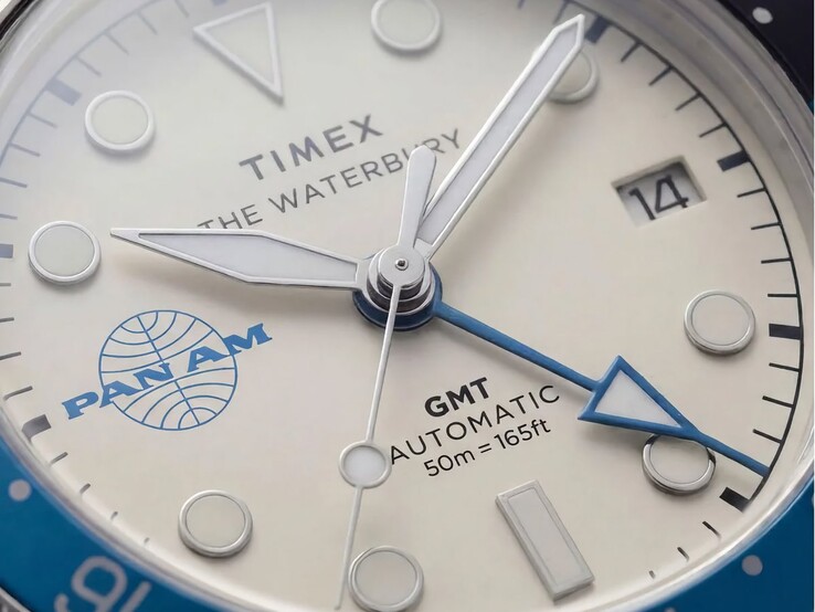 Zbliżenie na zegarek Timex Pan Am Waterbury Automatic GMT przedstawiające jego srebrno-białą tarczę, świecące znaczniki godzin, okienko datownika oraz logo Pan Am.