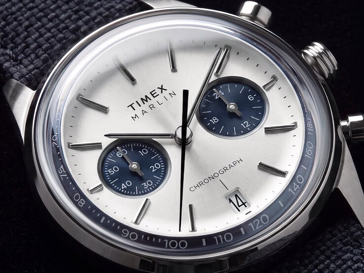 Zbliżenie na chronograf Timex Marlin Jet TW2Y89900 przedstawiające jego srebrno-białą tarczę, granatowe tarcze pomocnicze, nakładane indeksy godzinowe, wskazówki typu baton, skalę tachymetryczną oraz okienko datownika.