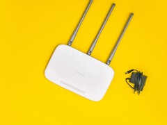 Biały router Wi-Fi z trzema antenami i zasilaczem na żółtym tle