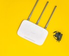 Biały router Wi-Fi z trzema antenami i zasilaczem na żółtym tle