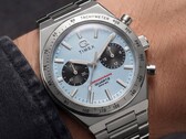 Zbliżenie na zegarek Timex Q Timex Continental Chronograph TW2Y92400 noszony na nadgarstku, wyposażony w lodowoniebieską tarczę w stylu CD z promienistym wzorem, czarne tarcze pomocnicze, srebrną ramkę z tachymetrem oraz zintegrowaną bransoletę ze stali nierdzewnej.
