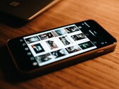 Smartfon leżący na drewnianym biurku, na którego wyświetlaczu widoczna jest siatka zdjęć