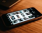 Smartfon leżący na drewnianym biurku, na którego wyświetlaczu widoczna jest siatka zdjęć