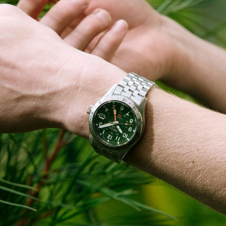 Widok z przodu zegarka Seiko 5 Sports Field GMT HDB001 z zieloną tarczą, nieruchomą 24-godzinną ramką ze stali nierdzewnej, pomarańczową wskazówką GMT oraz pięcioczęściową bransoletą ze stali nierdzewnej.