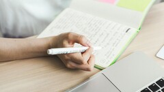 Osoba sporządza notatki w notatniku obok otwartego laptopa