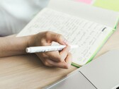 Osoba sporządza notatki w notatniku obok otwartego laptopa
