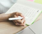 Osoba sporządza notatki w notatniku obok otwartego laptopa