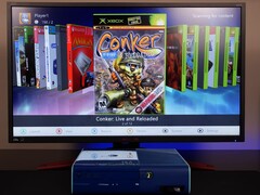 Zmodyfikowana niebieska konsola Xbox 360 z niestandardowym pulpitem homebrew na monitorze, wyświetlającym grę "Conker: Live and Reloaded" wraz z innymi tytułami na konsolę Xbox i emulatory. (Źródło obrazu: Modern Vintage Gamer na YouTube)