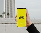 Dłoń trzymająca smartfon z dużym napisem „eSIM” na żółtym ekranie.