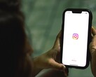 Kobieta trzymająca smartfon obiema rękami; na wyświetlaczu widoczny jest ekran startowy serwisu Instagram
