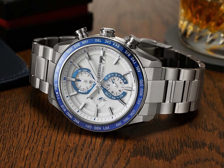 Chronograf Citizen Attesa AT8297-51L leżący na drewnianym stole, z granatową tarczą, detalami w kolorze różowego złota i czarną lunetą czasu światowego.