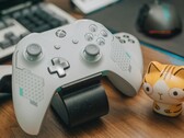 Biały kontroler Xbox spoczywający na drewnianym biurku obok małej figurki kota (źródło zdjęcia: FOX ^.ᆽ.^= ∫ via Pexels)