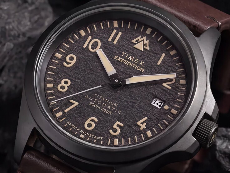 Zbliżenie na teksturowaną czarną tarczę zegarka Timex Expedition Field Post Titanium z cyframi arabskimi, świecącymi wskazówkami i znacznikami oraz okienkiem datownika.