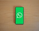 Smartfon na drewnianym biurku, na którego ekranie widoczny jest zielony ekran startowy aplikacji WhatsApp wraz z jej logo.