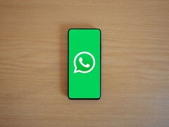 Smartfon na drewnianym biurku, na którego ekranie widoczny jest zielony ekran startowy aplikacji WhatsApp wraz z jej logo.