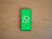 Smartfon na drewnianym biurku, na którego ekranie widoczny jest zielony ekran startowy aplikacji WhatsApp wraz z jej logo.